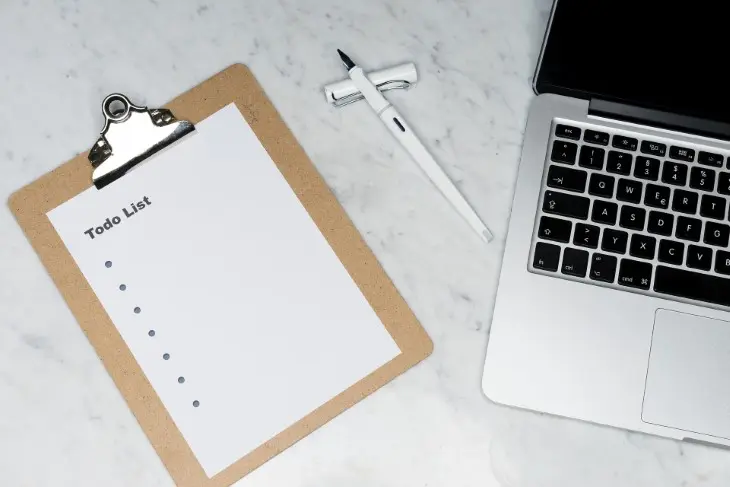 Klemmbrett mit To-Do-Liste, neben einem Stift und einem aufgeklappten Notebook.